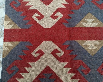 Puede incluir: Una alfombra roja, beige y gris con un borde de flecos. La alfombra tiene un diseño geométrico con un patrón repetitivo.