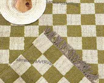 Puede incluir: Una alfombra a cuadros verdes y blancos con flecos. La alfombra está hecha de fibras naturales y tiene un aspecto rústico. El texto "SanwarryaArtRug" es visible en la imagen.