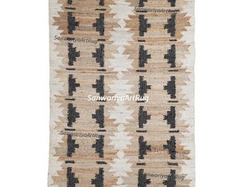 May include: A rectangular jute rug with a geometric pattern in beige, brown, and black. The rug has a repeating design of stylized crosses and triangles, with fringed edges. The text "SanwariyaArtRug" is visible.