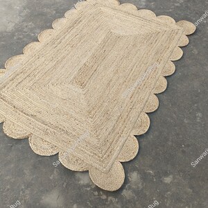 May include: A natural fiber rug with a scalloped edge. The rug is made of jute and has a light brown color.