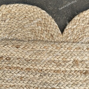 May include: A close-up of a natural fiber rug with a braided design. The rug is made of jute and has a light brown color. The rug is in the shape of a heart.