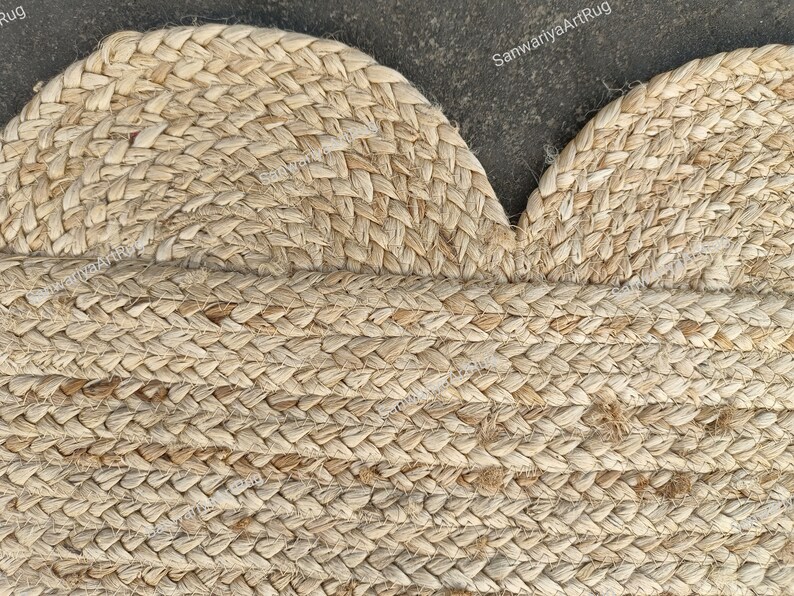 May include: A close-up of a natural fiber rug with a braided design. The rug is made of jute and has a light brown color. The rug is in the shape of a heart.