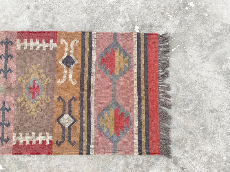 May include: A colorful rug with geometric patterns in shades of red, brown, gray, and beige. The rug has a fringe on the right side.
