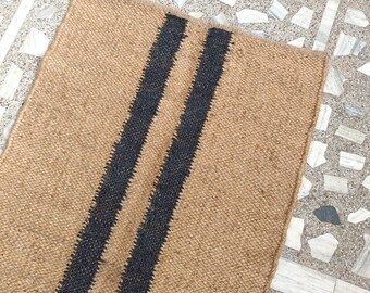 May include: A brown jute rug with two black stripes running down the length of the rug.