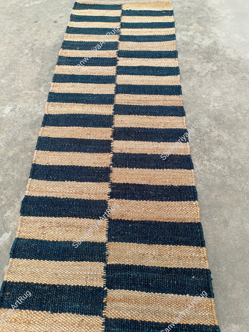 May include: A striped jute rug with alternating black and natural colored stripes. The rug is woven with a simple pattern and has a natural, rustic look.