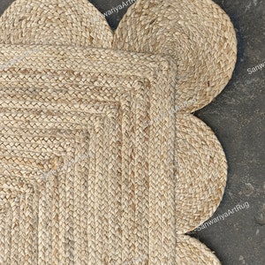May include: A natural fiber rug with a flower shape. The rug is made of woven jute and has a light brown color. The rug has five rounded petals and a square center.