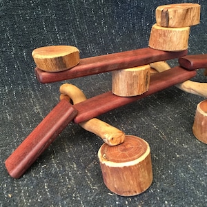 May include: A wooden toy construction set featuring natural wood pieces and red stained wood pieces. The pieces are stacked and balanced to create a unique structure.