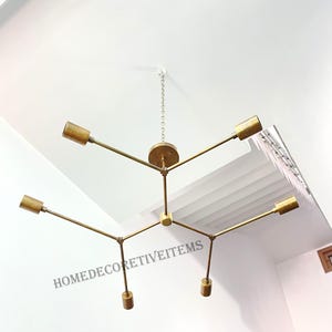 May include: A gold metal chandelier with six light bulbs. The chandelier has a geometric design with multiple arms extending from a central point. The chandelier is hanging from a chain.