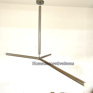 Könnte beinhalten: Ein moderner, silberfarbener dreiflügeliger Kronleuchter mit einer zentralen Hängestange und drei Glühbirnen an den Enden der Arme. Der Kronleuchter ist an der Decke befestigt.