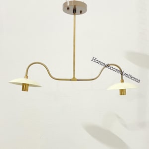 Op de afbeelding: Een messing hanglamp met twee lampen, gebogen armen en witte lampenkappen. De lamp heeft een eenvoudig, modern ontwerp.