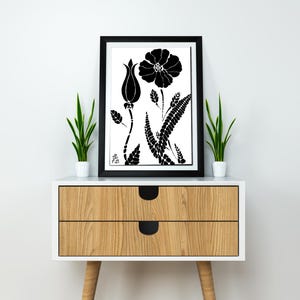 Puede incluir: Impresión en blanco y negro de una flor estilizada con un solo capullo y hojas. La impresión está enmarcada y se muestra en una mesita de noche de madera con dos cajones.