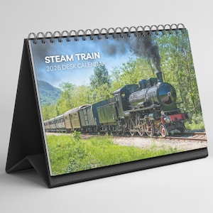 May include: A desk calendar featuring a steam train image. The calendar has a black stand and a spiral binding. The image shows a black steam train with green train cars traveling on a track through a green forest. The text "STEAM TRAIN 2026 DESK CALENDAR" is printed on the top.