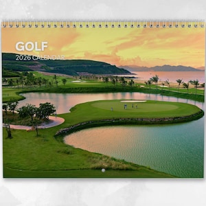 Könnte beinhalten: Ein 2026 Golfkalender mit Spiralbindung, der einen Golfplatz mit See und grünen Fairways zeigt. Das Wort "GOLF" steht oben. Das Bild zeigt einen Golfplatz mit Palmen und einem Gewässer vor dem Hintergrund eines Sonnenuntergangs.