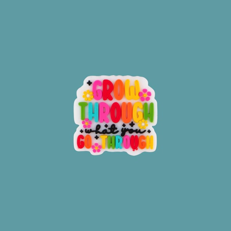 May include: A white, flower-shaped charm with the words "GROW THROUGH what you GO THROUGH" in colorful, bubble letters. The charm has a teal background.