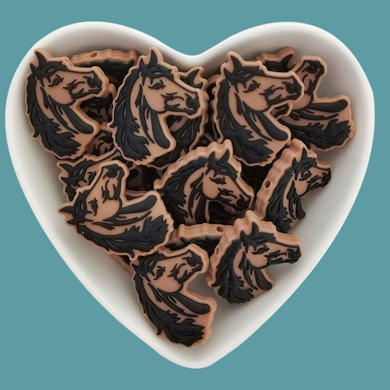 May include: A bowl filled with brown and black horse head shaped beads. The beads are made of silicone and have a glossy finish.