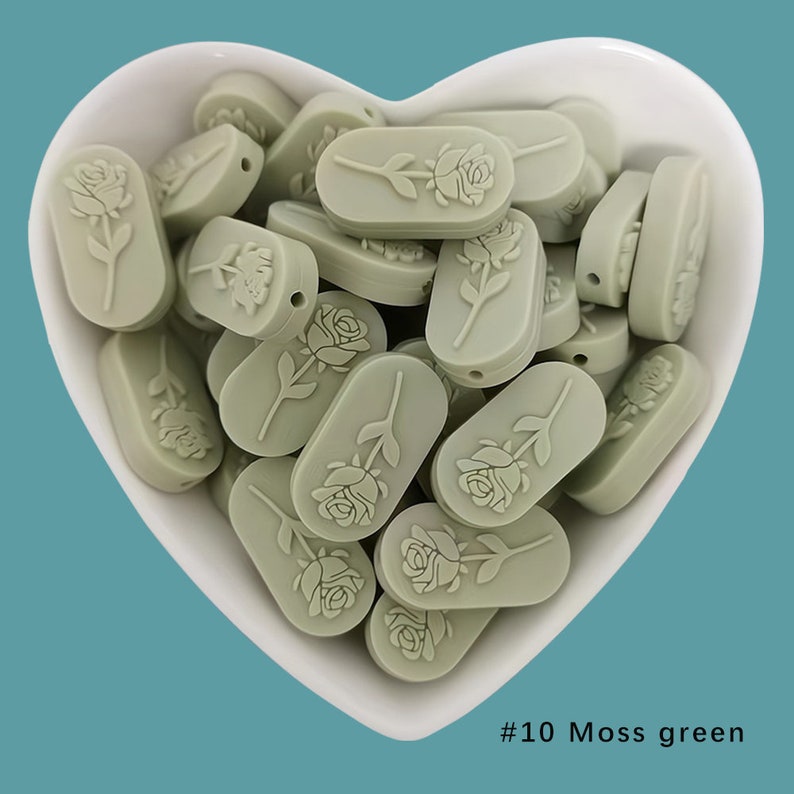 Op de afbeelding: Een kom gevuld met mosgroene siliconen kralen, elk met een reli&euml;f van een roos. #10 Mosgroen.