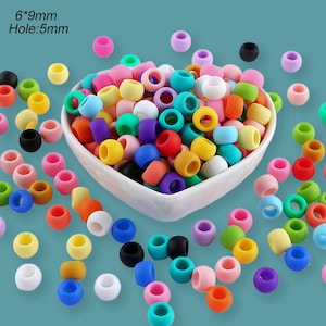 May include: A collection of colorful, round beads in various shades, including pink, yellow, blue, green, and purple. The beads are scattered around a white bowl and on a teal surface. Text on the image reads: 6*9mm Hole:5mm.