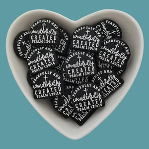 Puede incluir: Un bol blanco en forma de corazón lleno de abalorios de silicona negros y blancos. Cada abalorio tiene el texto "Fearfully and Wonderfully Created Psalm 139:14".