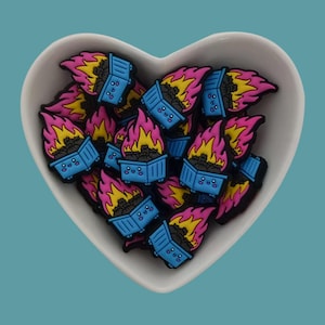 Könnte beinhalten: Eine herzförmige Schale gefüllt mit kleinen, blauen und gelben, feuerspeienden, Cartoon-Mülleimern mit fröhlichen Gesichtern. Die Mülleimer sind aus Gummi und eine lustige und skurrile Dekoration.