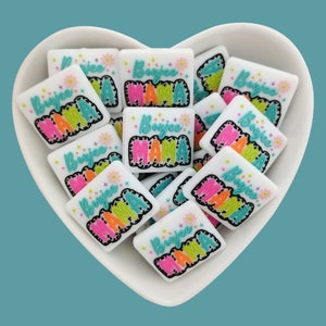 May include: A white heart-shaped bowl filled with colorful square-shaped resin charms. Each charm features the text "Boujee Mama" in a bold, colorful font with a black outline.