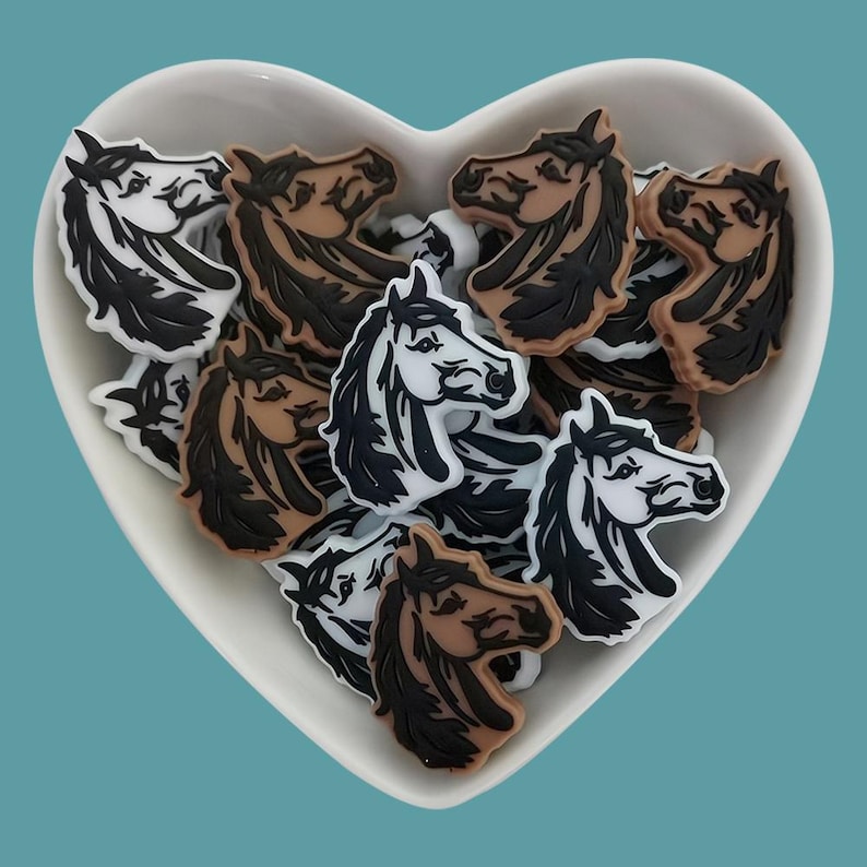 May include: A bowl filled with horse head charms in brown, white, and black. The charms are made of plastic and have a glossy finish.