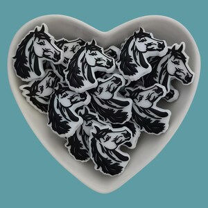 May include: A white heart-shaped dish filled with black and white horse head charms. The charms are made of a smooth, glossy material and have a detailed design.