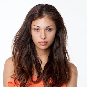 Puede incluir: Una joven con el pelo largo y castaño, lleva una camiseta naranja brillante sin mangas, mira directamente a la cámara con una expresión neutral.