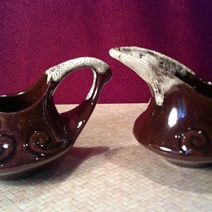 May include: A brown and white ceramic creamer and sugar set with a swirl design. The creamer has a handle and a spout. The sugar bowl has two handles.