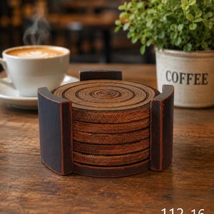 Pu&ograve; includere: Una pila di sei sottobicchieri circolari in legno con finitura a venature naturali, inseriti in un supporto in legno marrone scuro con finitura anticata. I sottobicchieri presentano motivi ad anelli concentrici. Il testo 112-16 &egrave; visibile.