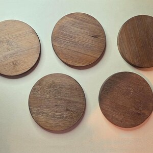 Pu&ograve; includere: Cinque sottobicchieri circolari in legno disposti a motivo. Ogni sottobicchiere presenta una venatura del legno naturale distinta in varie tonalit&agrave; di marrone, dal beige chiaro a un tono noce pi&ugrave; profondo, con una superficie liscia e piatta.