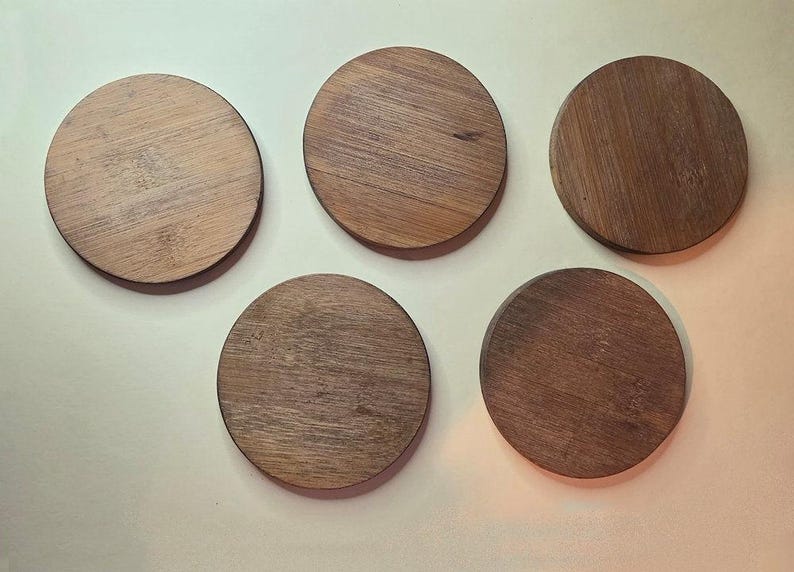 Pu&ograve; includere: Cinque sottobicchieri circolari in legno disposti a motivo. Ogni sottobicchiere presenta una venatura del legno naturale distinta in varie tonalit&agrave; di marrone, dal beige chiaro a un tono noce pi&ugrave; profondo, con una superficie liscia e piatta.