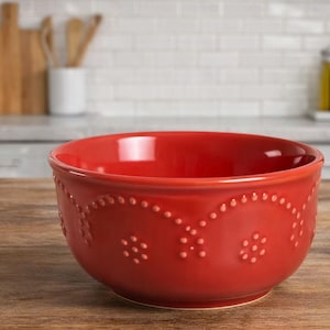 May include: A red ceramic bowl with a decorative dotted pattern around the rim. The bowl is set on a wooden surface. Kitchenware and serving bowl.