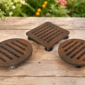May include: Three dark brown wooden trivets with slatted designs, including one square and two oval shapes. Each trivet is supported by small, dark, rounded feet. The text 164-5 is visible in the bottom right corner of the image.