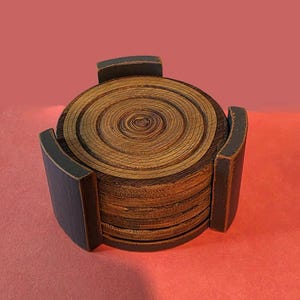 Pu&ograve; includere: Una pila di sottobicchieri circolari in legno con venature visibili, inseriti in un supporto in legno nero con finitura opaca. I sottobicchieri presentano anelli concentrici che ricordano gli anelli di crescita degli alberi.