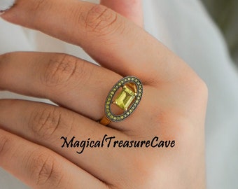 May include: A gold-toned ring with a rectangular yellow gemstone at the center, surrounded by smaller, circular stones. The ring is on a hand, with the text "Magical Treasure Cave" visible.