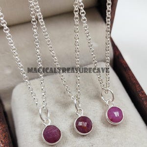 May include: Three silver necklaces featuring round, faceted, deep pink gemstone pendants. Each pendant is securely attached to a delicate silver chain with a small jump ring. The text MAGICALTREASURECAVE is visible in the centre of the image.