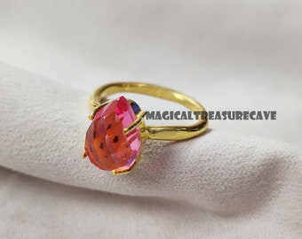 May include: A gold ring with a pink pear-shaped gemstone. The ring is set with a small blue stone on the side.