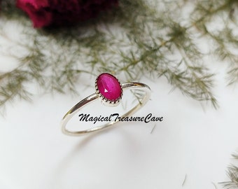 Puede incluir: Un anillo de plata con una piedra ovalada rosa engastada en un engaste de plata. El anillo está sobre una superficie blanca con follaje verde en el fondo.  MagicalTreasureCave está escrito en la imagen.