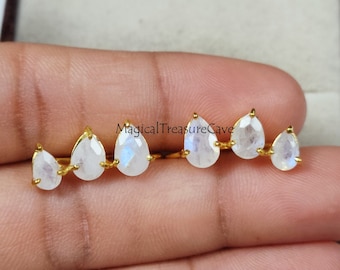 May include: A pair of gold-colored earrings featuring a series of pear-shaped, iridescent moonstone gems. The earrings are set in a linear arrangement, with each stone individually mounted on a thin gold bar. The text "Magical Treasure Cave" is visible.