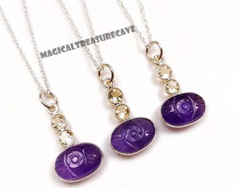 Op de afbeelding: Drie zilveren kettingen met amethist hangers. Elke hanger heeft een ovale vorm met een uitgesneden oogontwerp. De kettingen hebben ook kleine, ronde, geel getinte edelstenen. De tekst "MAGICALTREASURECAVE" is zichtbaar.