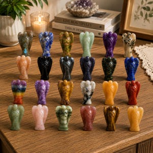 May include: A collection of small, carved angel figurines in various colors and materials, including marble and gemstones. The angels are displayed on a wooden surface, showcasing their detailed wings and serene expressions. The collection includes angels in shades of blue, green, purple, and orange.