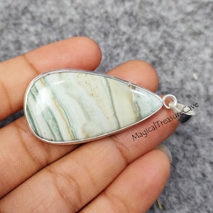 May include: A teardrop-shaped pendant with a green and white agate stone set in a silver frame. The pendant is on a hand, and the text "MagicalTreasureCave" is visible in the background.