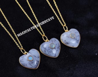 May include: Three heart-shaped pendants on gold-tone rope chains. Each pendant features a white stone with black dendritic inclusions and a small, round, blue-toned center stone. The text MAGICALTREASURECAVE is visible across the image.