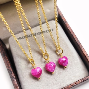 Op de afbeelding: Drie goudkleurige kettingkettingen met hartvormige, gefacetteerde, roze hangers. De kettingen worden gepresenteerd in een bruine doos. De tekst "MAGICALTREASURECAVE" is zichtbaar. Elke ketting heeft een kleine gouden kraal.