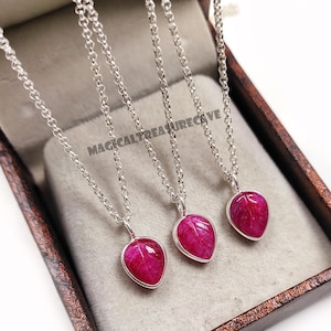 Può includere: Tre collane d'argento con pendenti a forma di goccia di colore rosa intenso. I pendenti hanno un aspetto strutturato e sono incastonati in una lunetta d'argento. Le collane sono esposte in un cofanetto marrone. Il testo "MAGICALTREASURECAVE" è visibile.