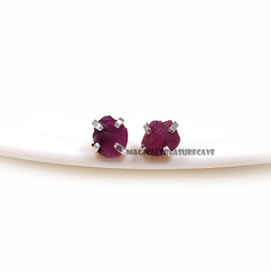 May include: A pair of silver stud earrings with small, raw ruby gemstones. The rubies are a deep, rich red color and have a natural, unpolished look.