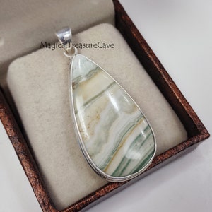May include: A silver pendant featuring a teardrop-shaped green and white agate stone with a swirling pattern. The pendant is in a brown velvet box.