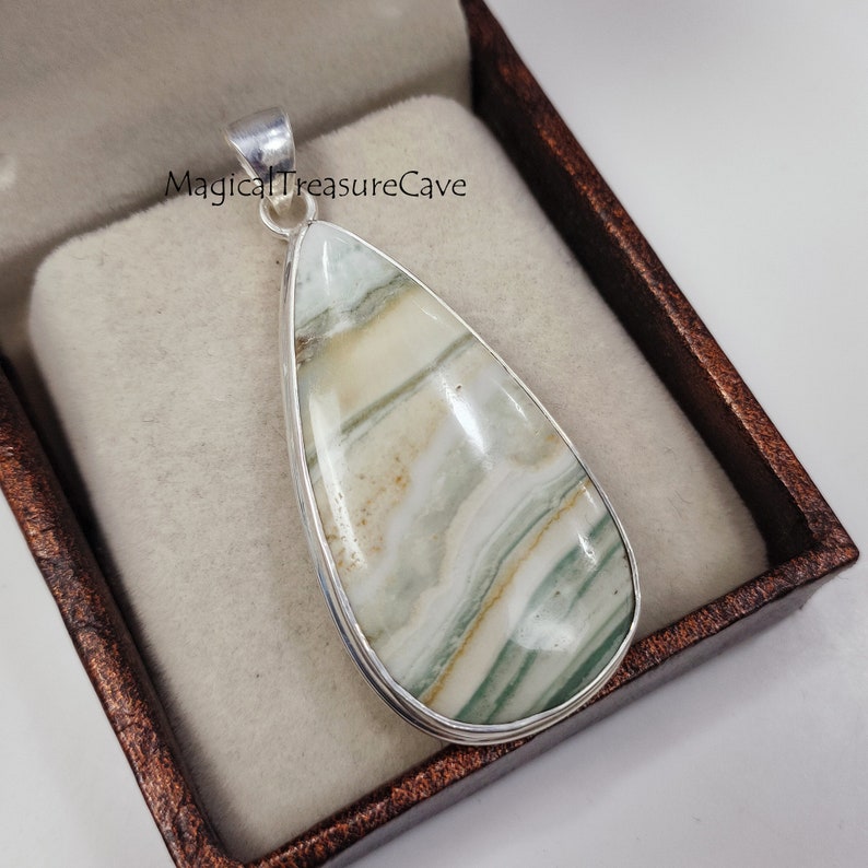 May include: A silver pendant featuring a teardrop-shaped green and white agate stone with a swirling pattern. The pendant is in a brown velvet box.