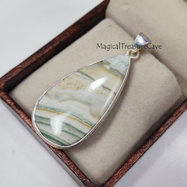 May include: A silver pendant featuring a teardrop-shaped green and white agate stone with a silver bail. The pendant is in a small, brown velvet box with the text "MagicalTreasureCave" printed on the box.