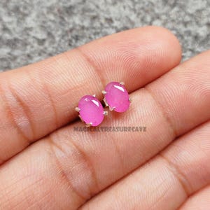 Op de afbeelding: Een paar ovale oorknopjes met roze edelstenen en zilverkleurige klauwen. De oorbellen worden gepresenteerd op een licht oppervlak. De tekst "MAGICALTREASURECAVE" is zichtbaar eronder.